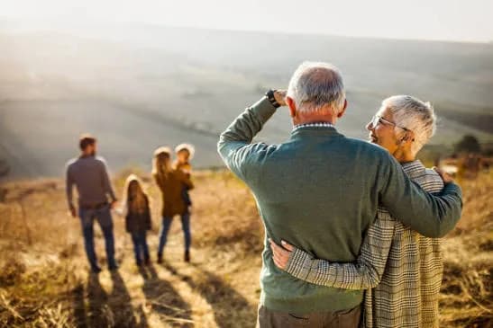 A senior couple looking out over a sunlit field toward their family